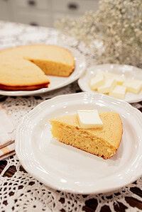 sourdough discard cornbread slice with butter on white plate with full cornbread in background